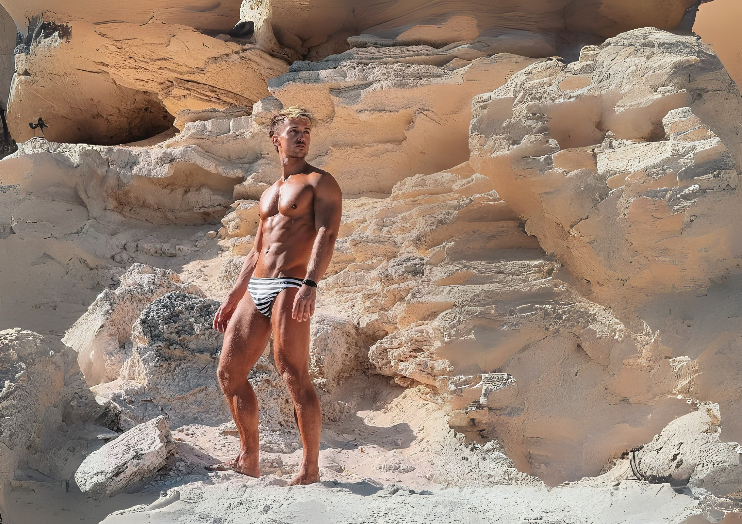 Man in swimwear standing on rocky terrain with sandstone formations in the background
